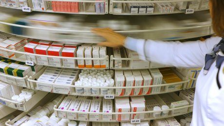 Apotekhyller fylt med medisinesker, og en person i hvit uniform som roterer et hyllesystem.