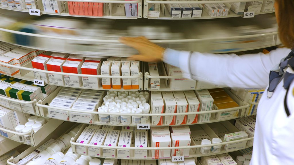 Apotekhyller fylt med medisinesker, og en person i hvit uniform som roterer et hyllesystem.