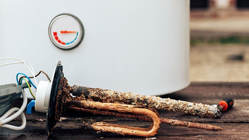 Rustne deler ligger foran en hvit varmtvannsbereder.