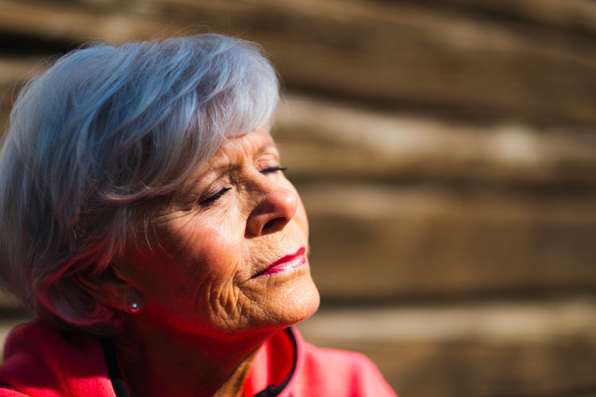 Nærbilde av ansiktet til en gråhåret, eldre kvinne som har øynene lukket og hviler i solveggen