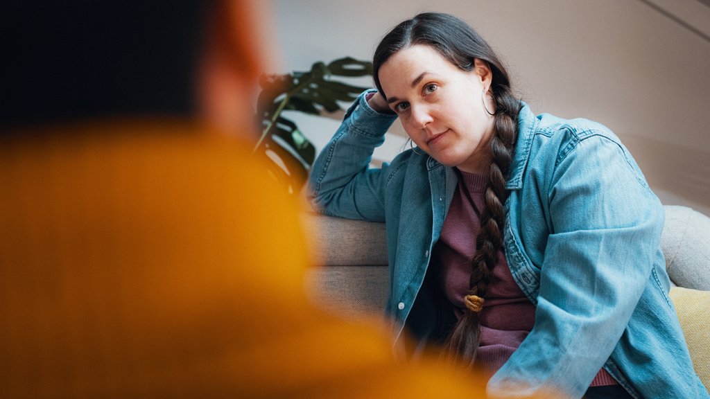 Person sitter i en sofa og lytter i en samtale, med avslappet holdning.