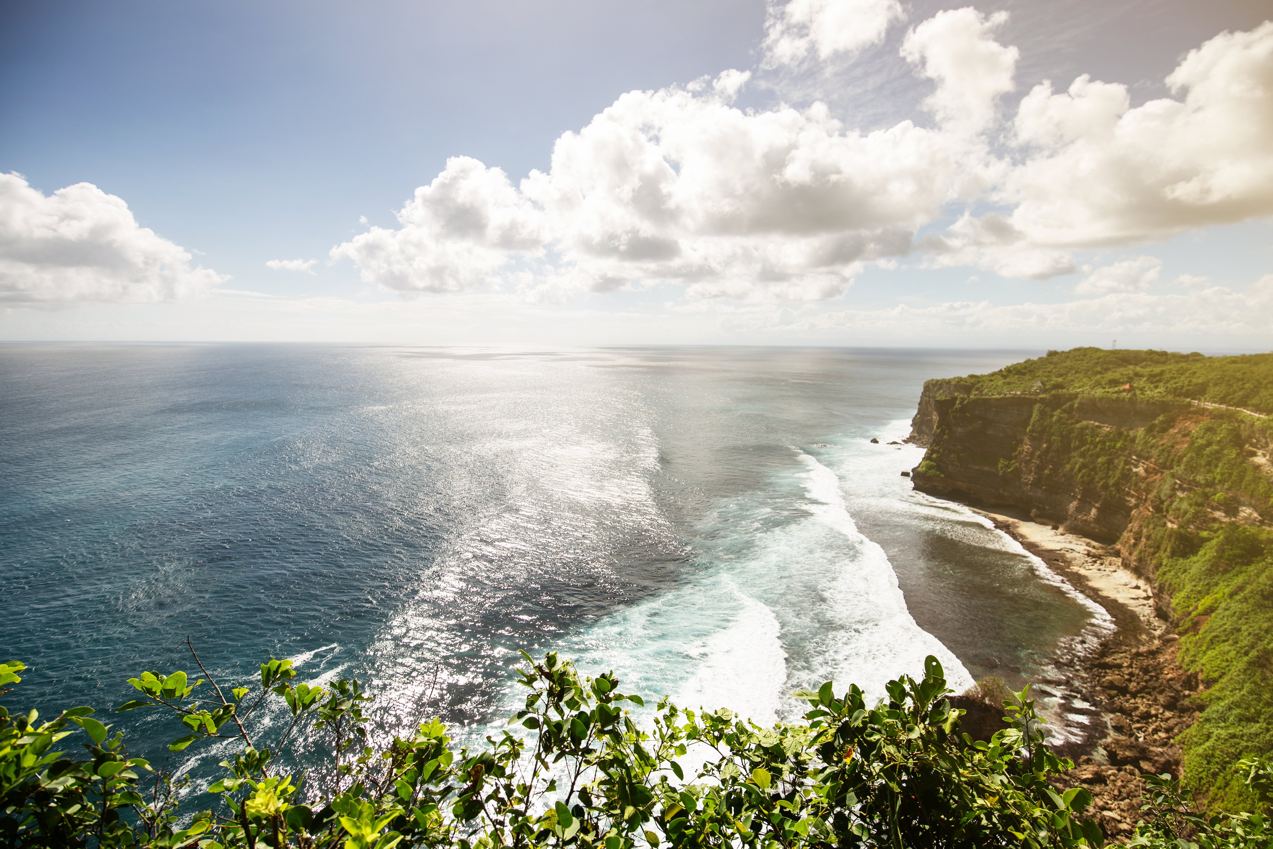 Utsikt over havet med bølger som slår mot en klippe og grønn vegetasjon i forgrunnen.