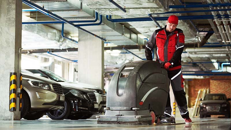 En mann bruker gulvvaskemaskin i en parkeringskjeller.