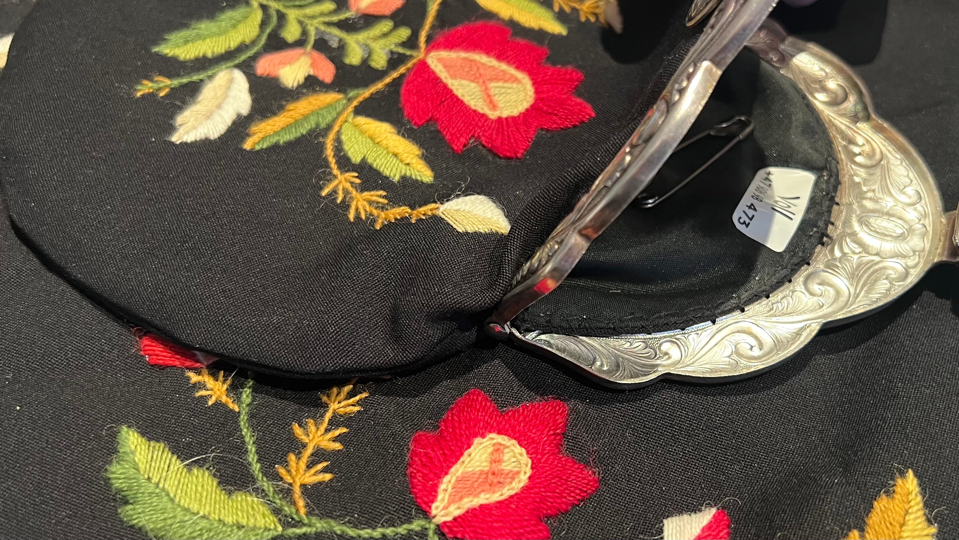 Nærbilde av en bunadsveske med navnelapp og sikkerhetsnål festet på innsiden