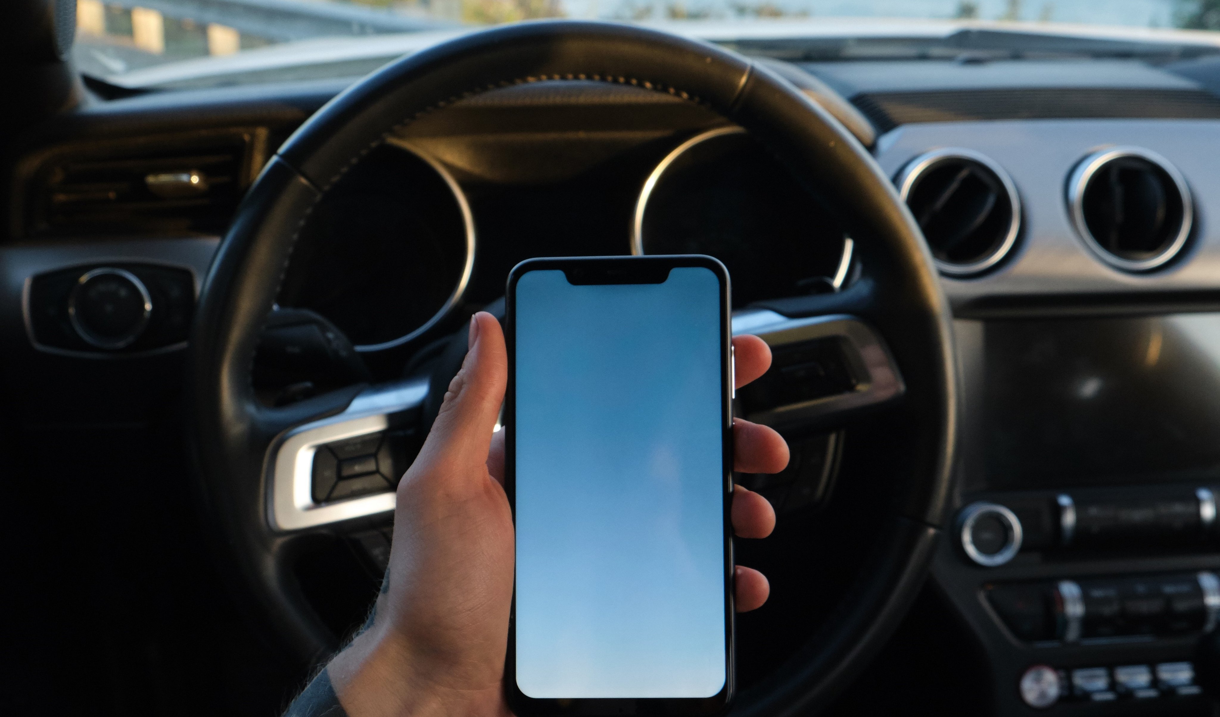 En mann holder en mobiltelefon mens han kjører bil.