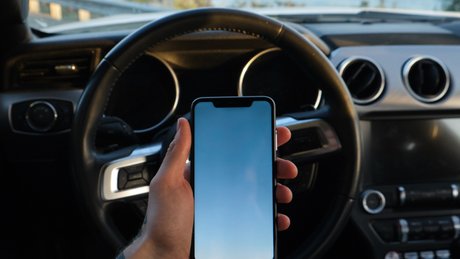 En mann holder en mobiltelefon mens han kjører bil.