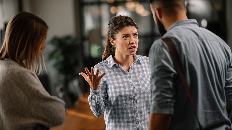 Tre kollegaer står sammen. Hun ene ser frustrert ut og slår ut med armene.