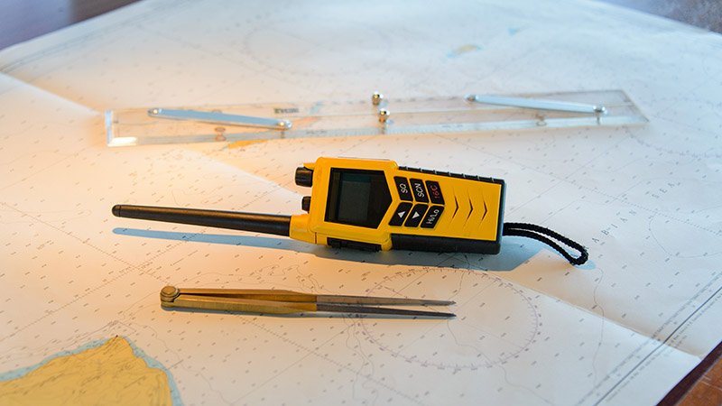 Sjøkart med navigasjonsverktøy, inkludert en gul håndholdt VHF-radio, en passer og en parallell linjal.