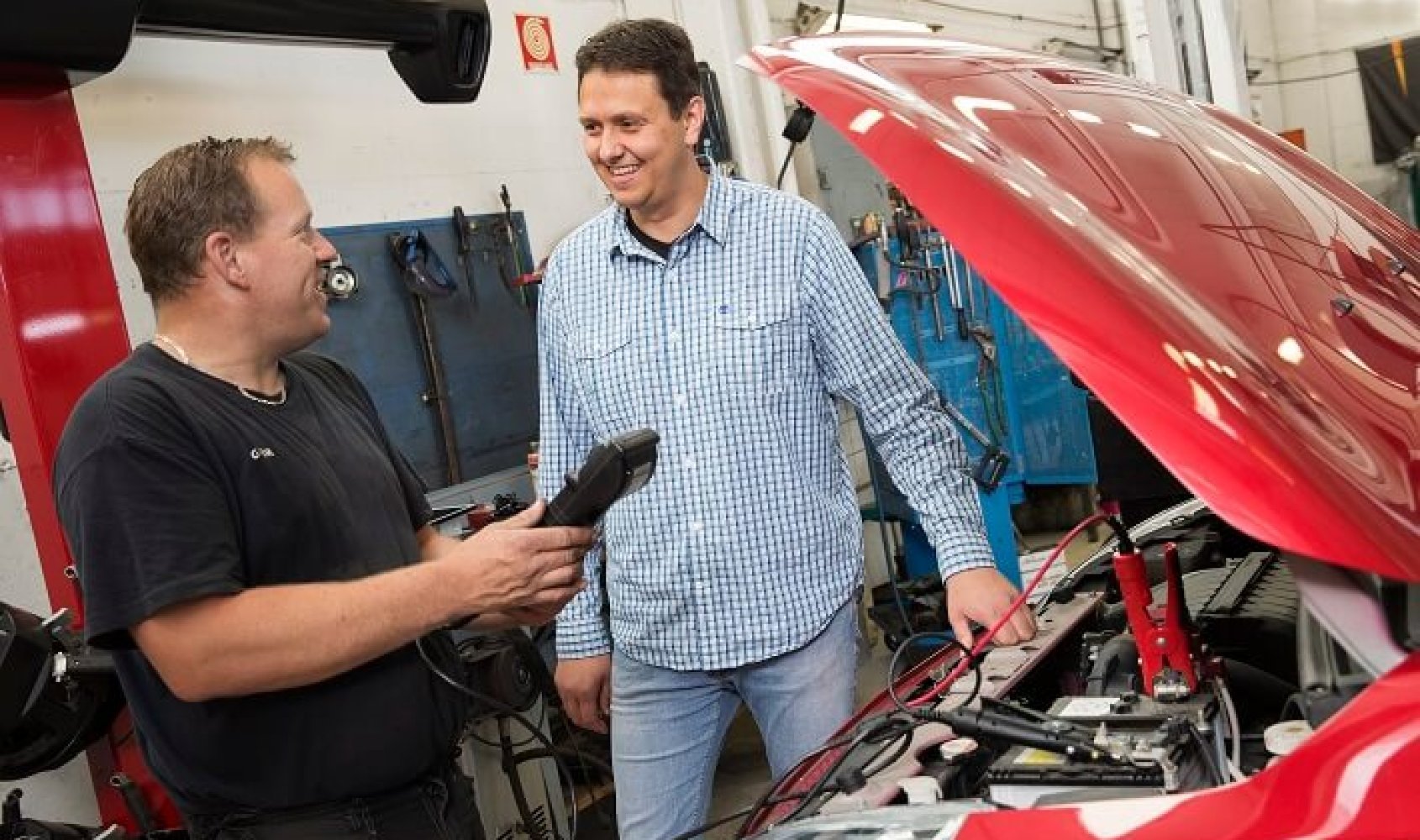 Jan Fleinsjø står ved en bil med åpent panser mens en ansatt på et verksted holder et diagnoseverktøy.