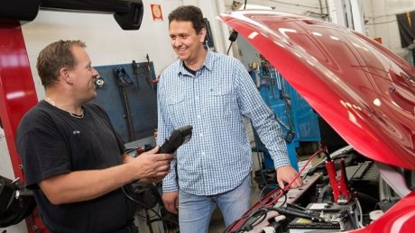 Jan Fleinsjø står ved en bil med åpent panser mens en ansatt på et verksted holder et diagnoseverktøy.