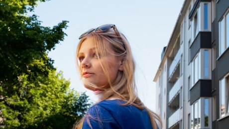 En ung jente med solbriller på hodet og langt hår står på gata og snur seg halvveis bakover.