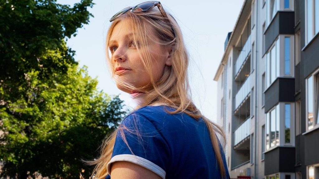 En ung jente med solbriller på hodet og langt hår står på gata og snur seg halvveis bakover.