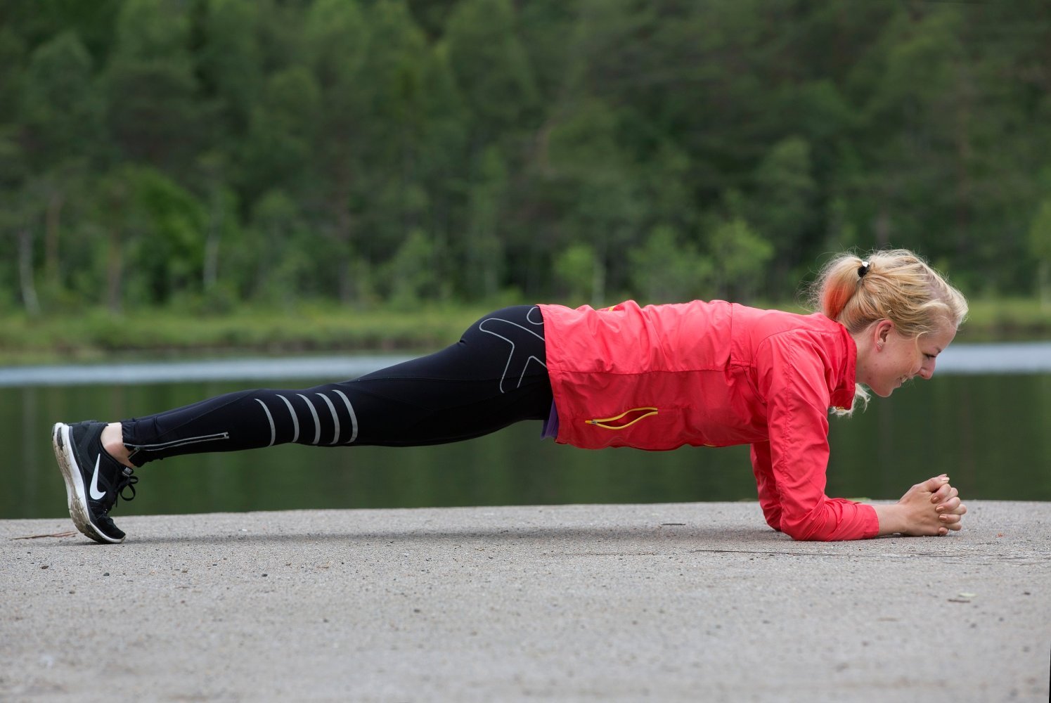 En kvinne gjør plankeøvelse utendørs ved et vann.