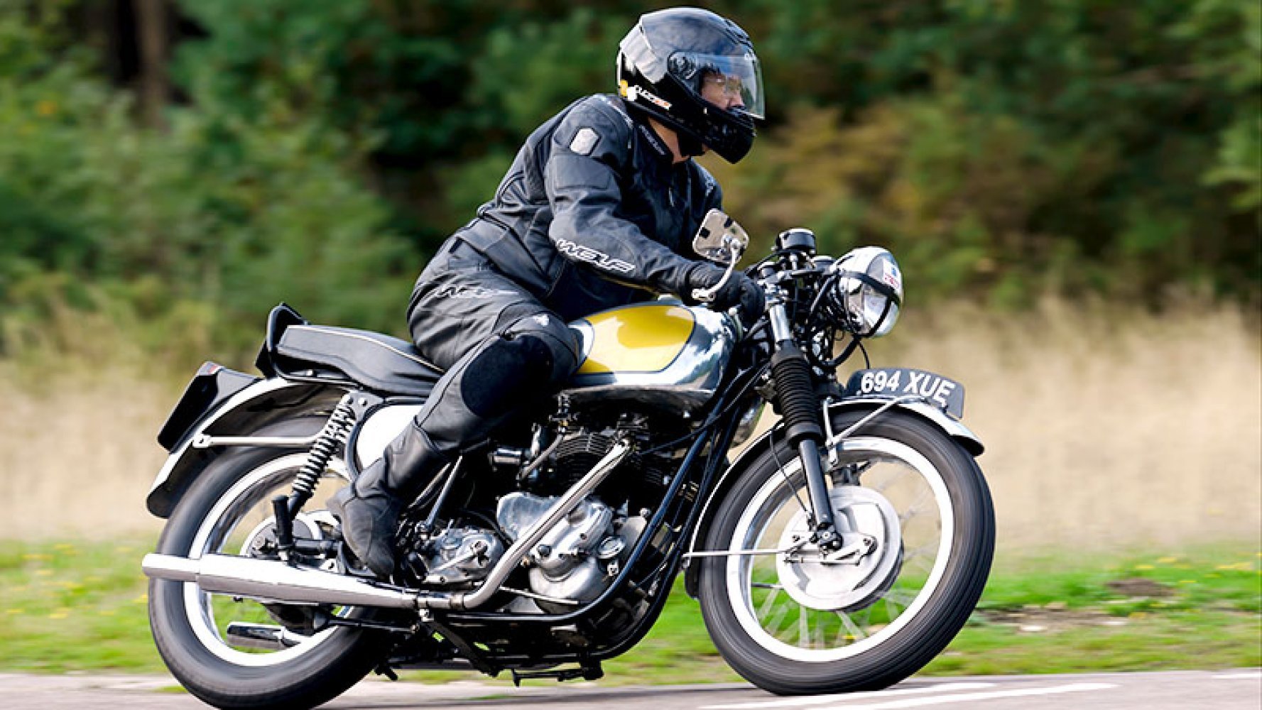 Mann i motorsykkelutstyr kjører en klassisk motorsykkel på landevei.