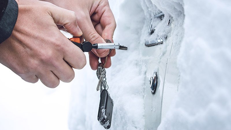 Hender bruker bilnøkkel i en lås på en snødekt bil.