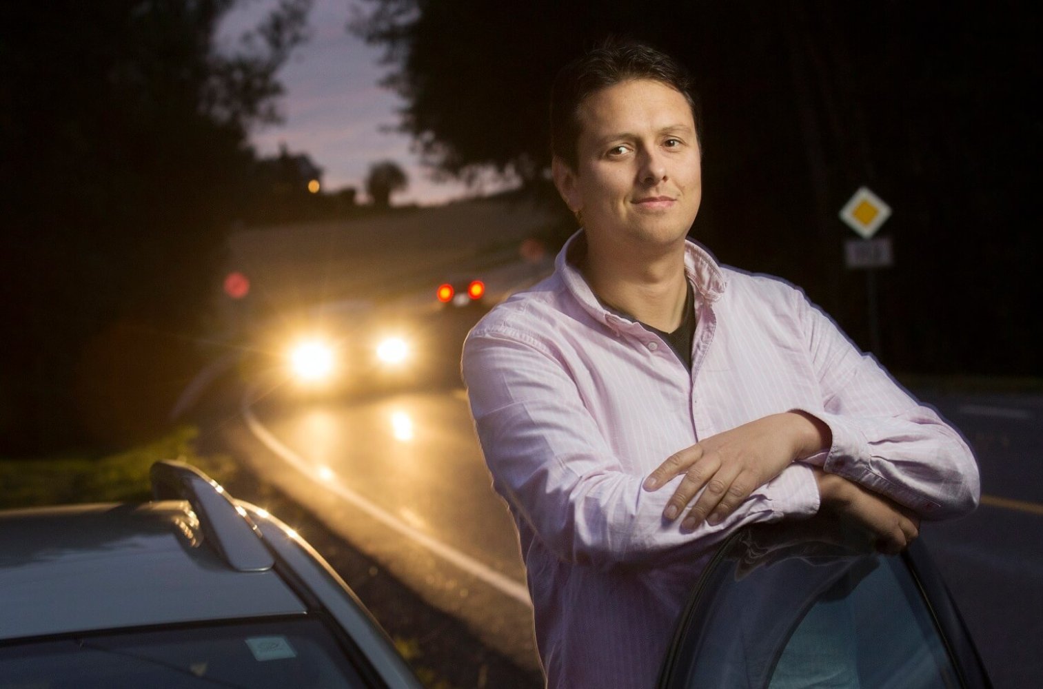 Jan Fleinsjø står og lener seg på en bil, parkert langs en bilvei i mørket.