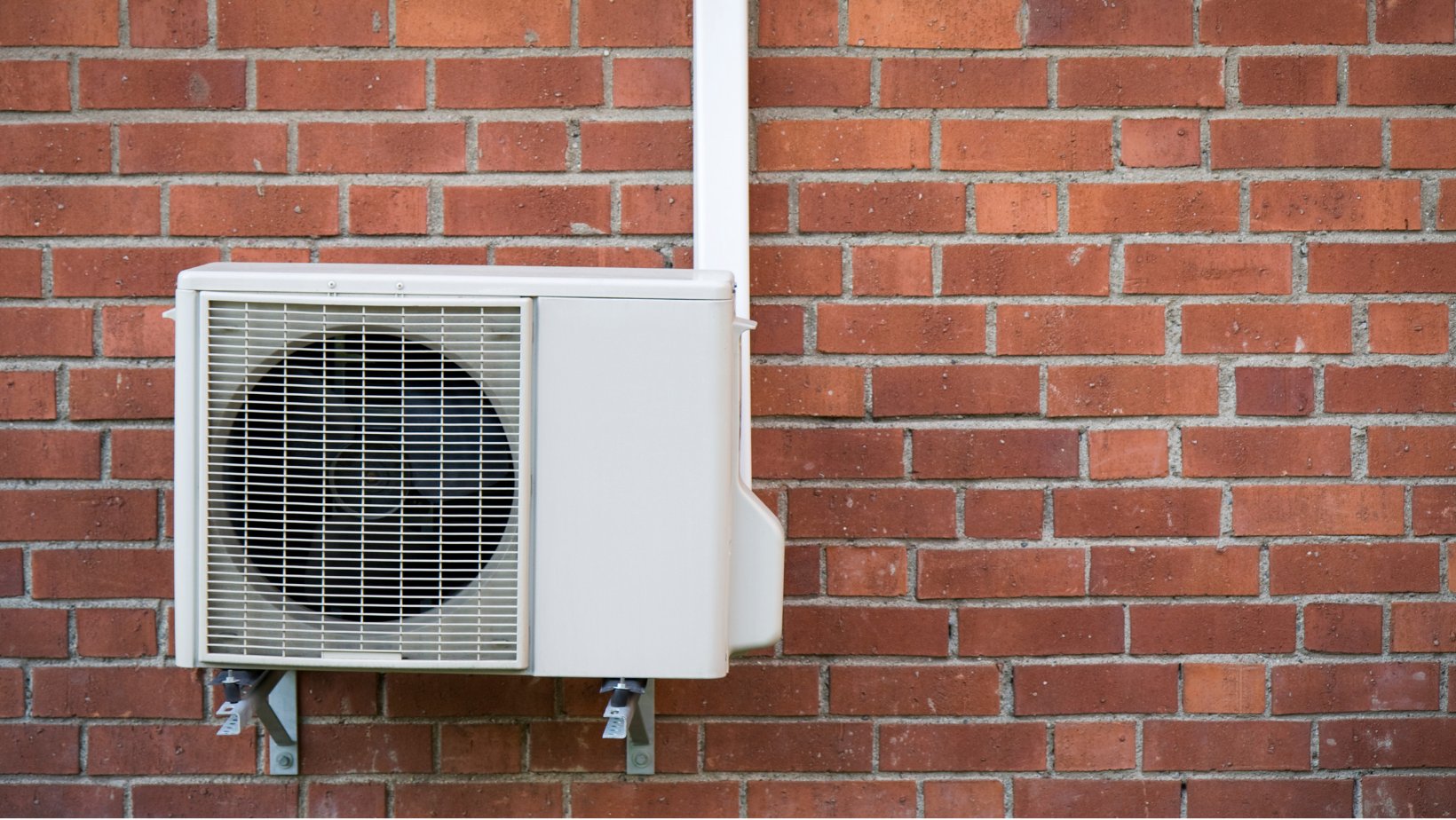 Hvit luft-til-luft-varmepumpe festet på utsiden av en rød mursteinsvegg.