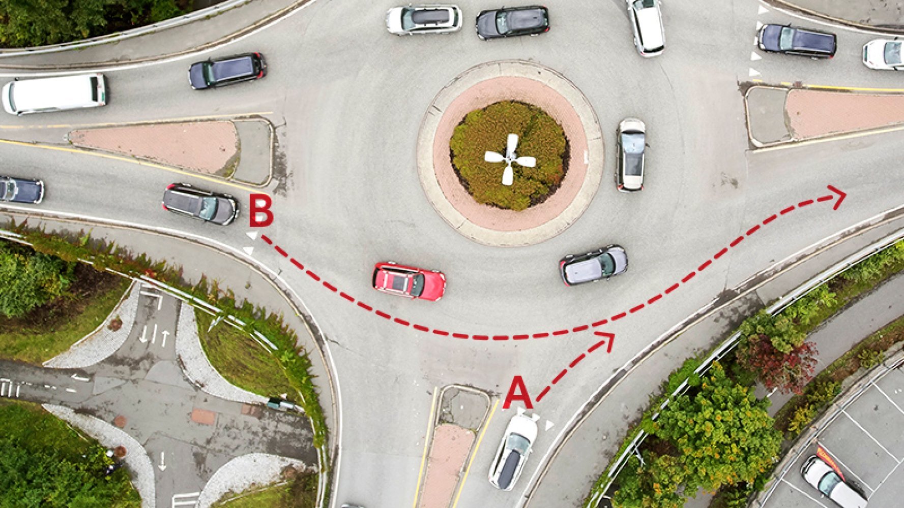 Oversiktsbilde av en rundkjøring med røde stiplete piler som viser kjøreruter merket A og B.