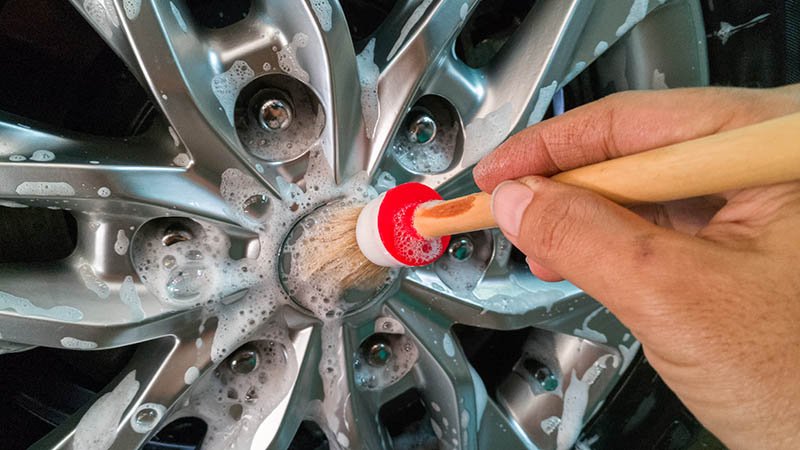 En hånd rengjør felgen på et bildekk med såpe og en liten kost