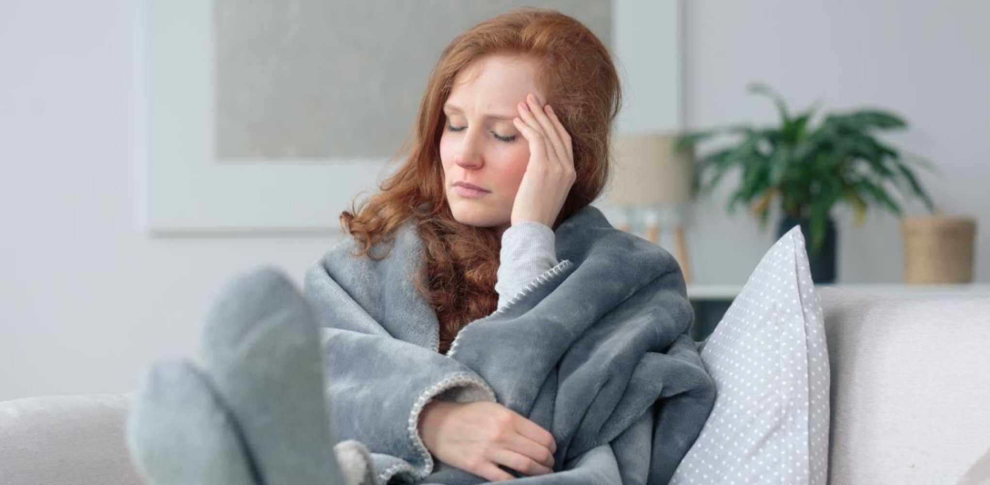 En rødhåret dame sitter intullet i fleecepledd og holder seg til hodet.