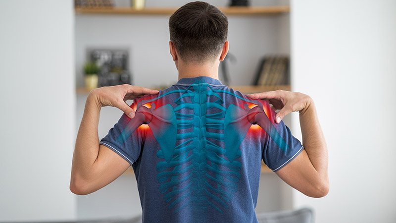 En person sett bakfra løfter armene mens en illustrasjon viser smerteområder rundt skuldrene og øvre rygg.