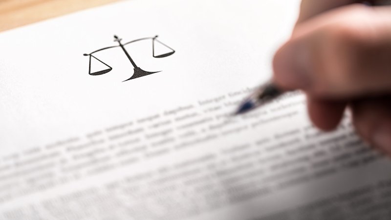 Dokument med juridisk symbol og hånd som skriver med penn.
