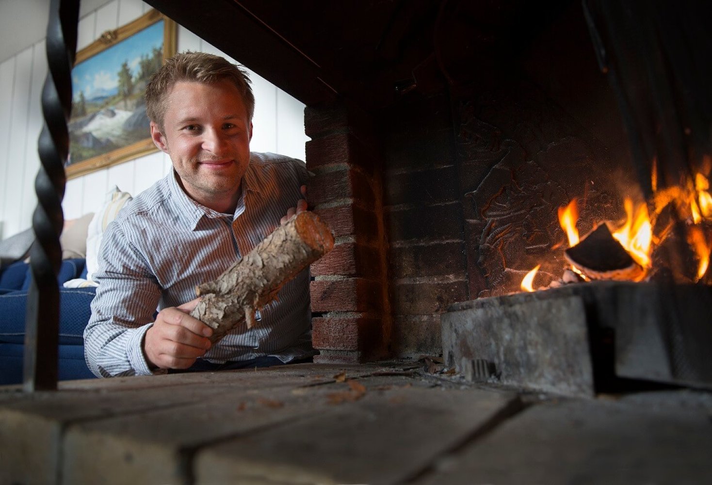 En mann holder en vedkubbe i hånden som han skal til å legge inn i bålet i peisen.