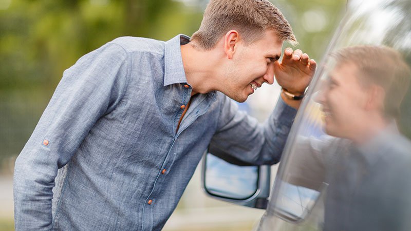 Mann som lener seg mot en bil og kikker inn gjennom sidevinduet.