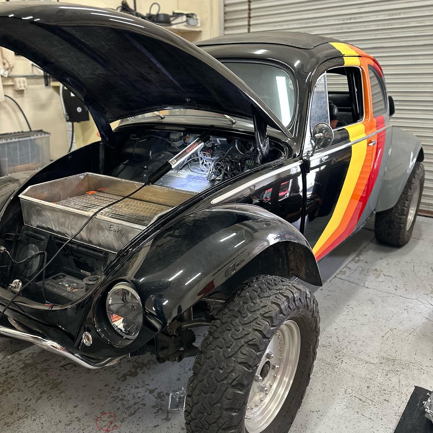 Volkswagen Boble med hevet panser som viser elektrisk motor og komponenter, med fargerike striper på siden.