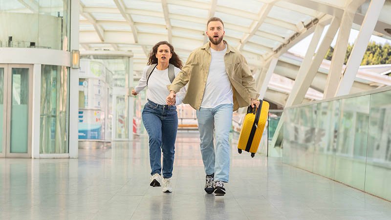 Mann og dame går gjennom flyplassterminal, ser stresset ut. 