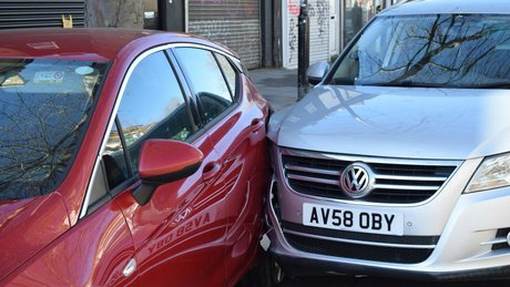 En sølvgrå Volkswagen har kjørt inn i siden på en rød bil.