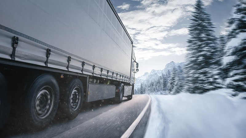 En semitrailer kjører på en vintervei i skogen.