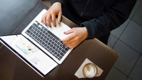 Hender som bruker laptop ved et bord med kaffekopp og notater.