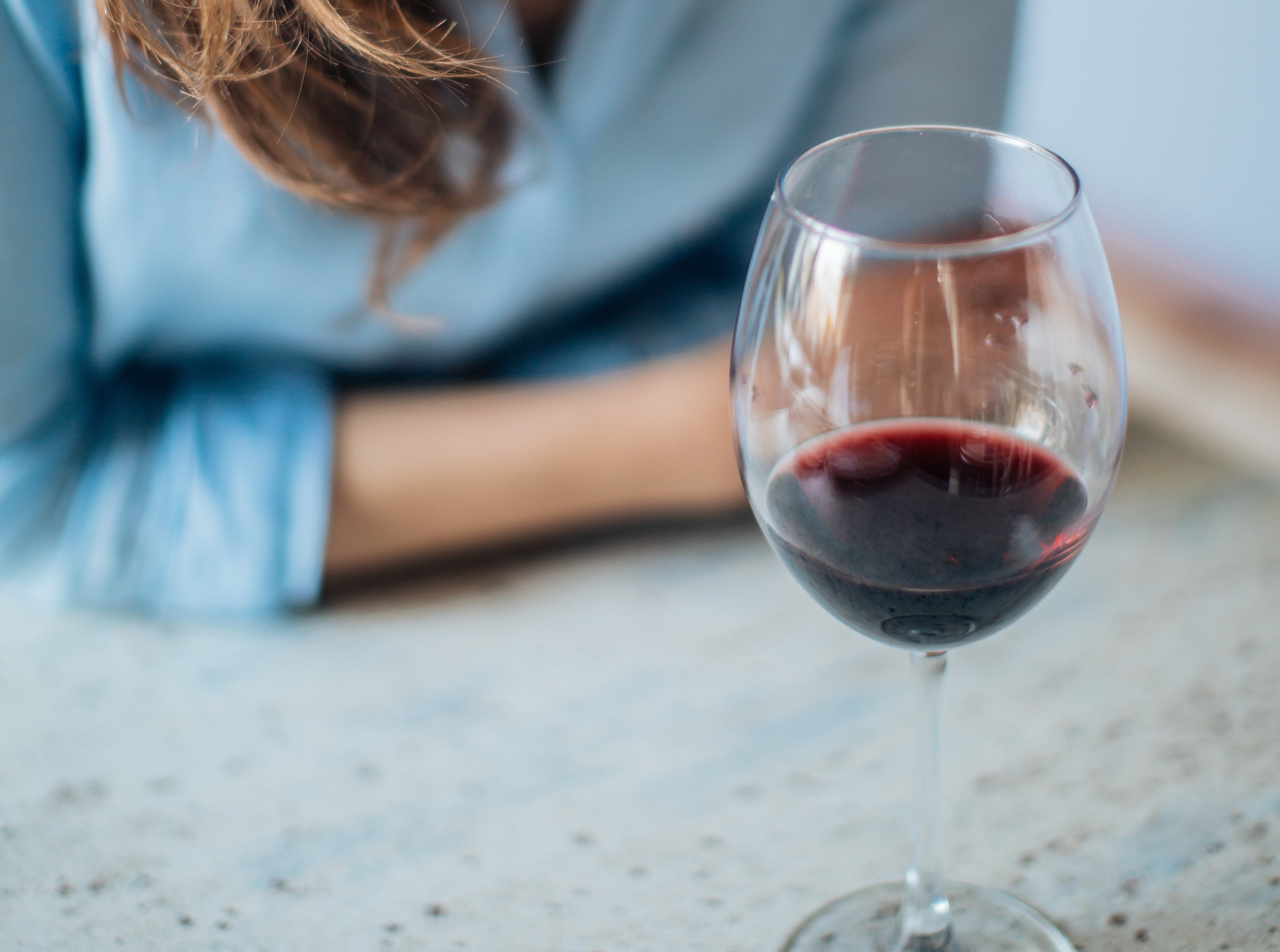 Et halvfullt vinglass. En kvinne sitter i bakgrunnen.