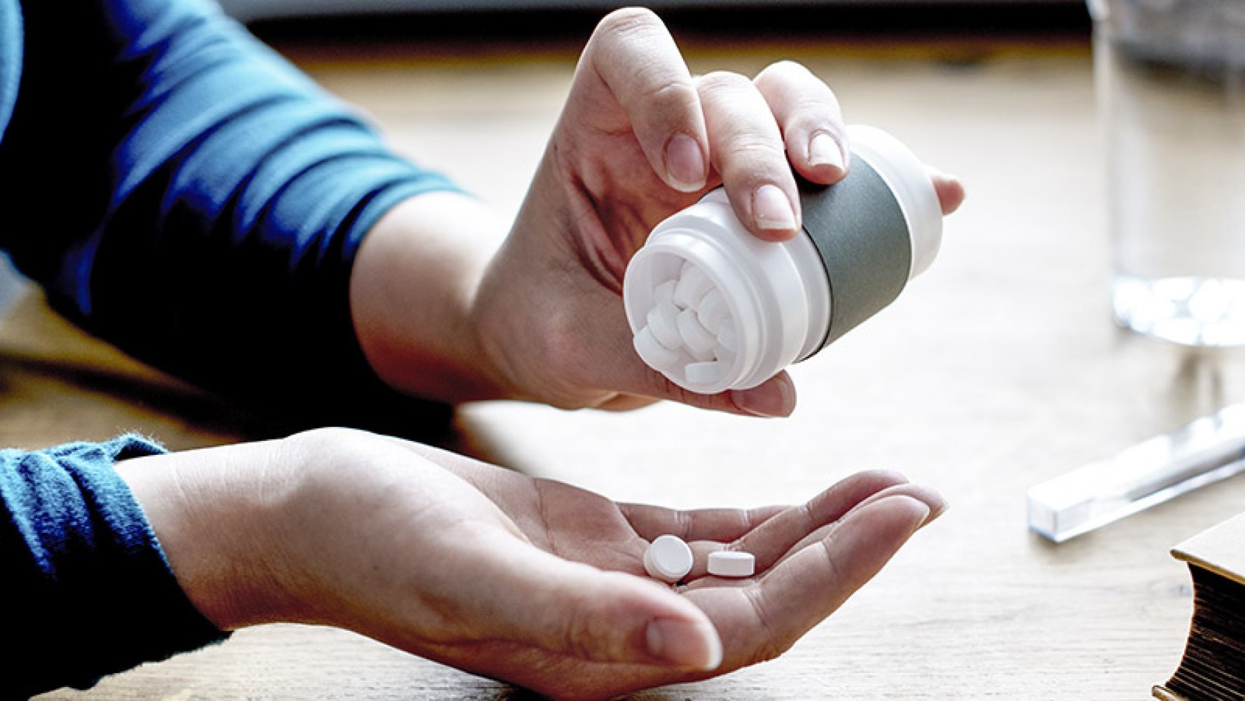 Person heller hvite tabletter fra en beholder i hånden.