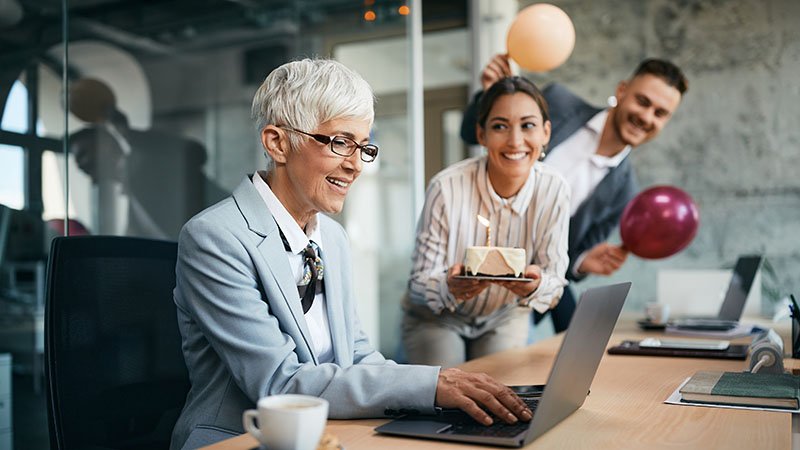 En ansatt blir feiret med kake og ballonger av to kolleger.