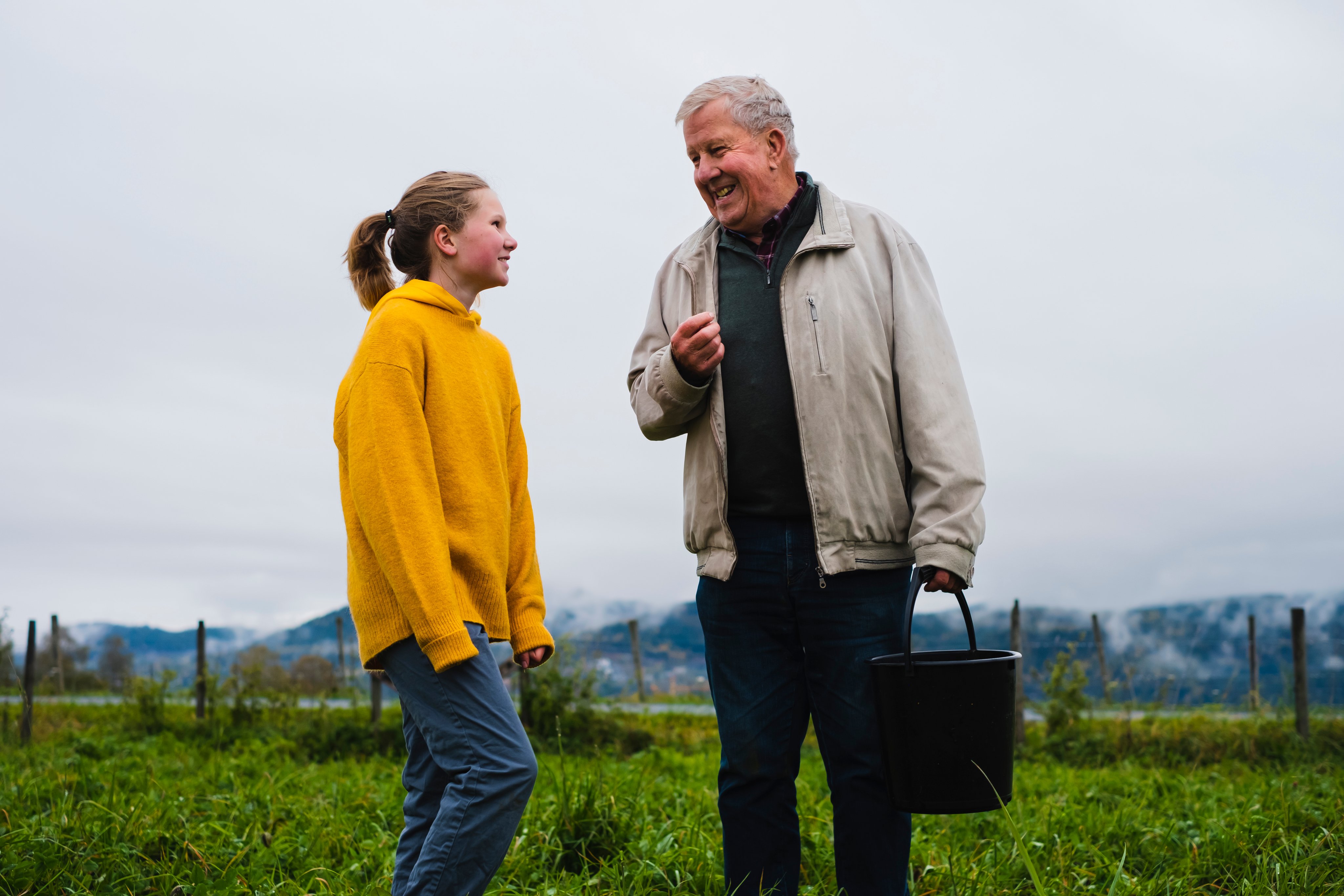 Barnebarn og bestefar prater sammen på åkeren.