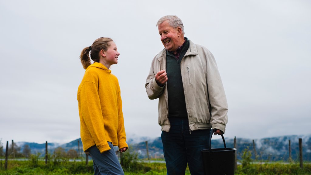 Barnebarn og bestefar prater sammen på åkeren.