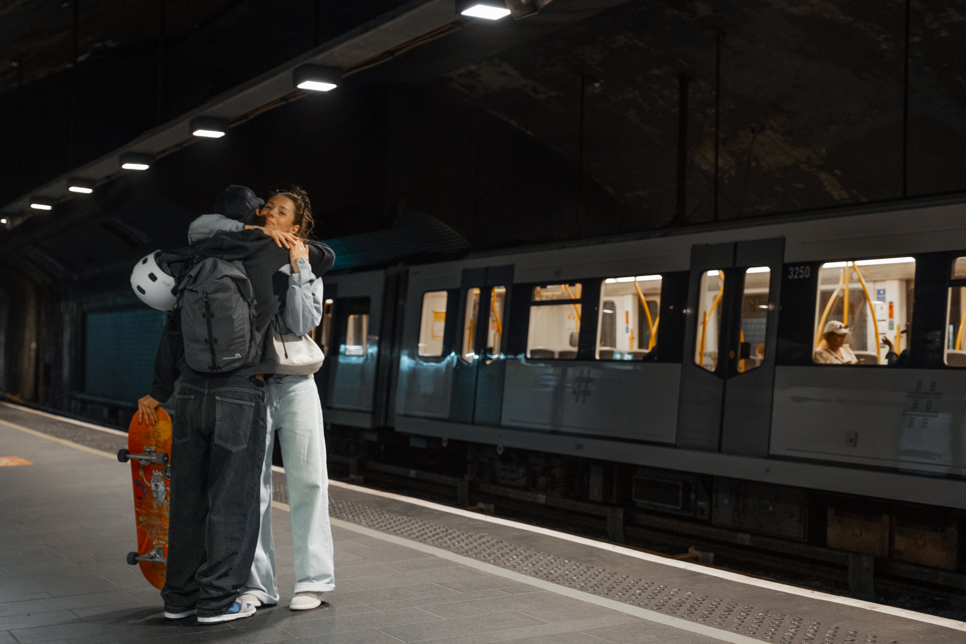 Et ungt kjærestepar klemmer hverandre på t-banestasjonen. I bakgrunnen er en t-bane.