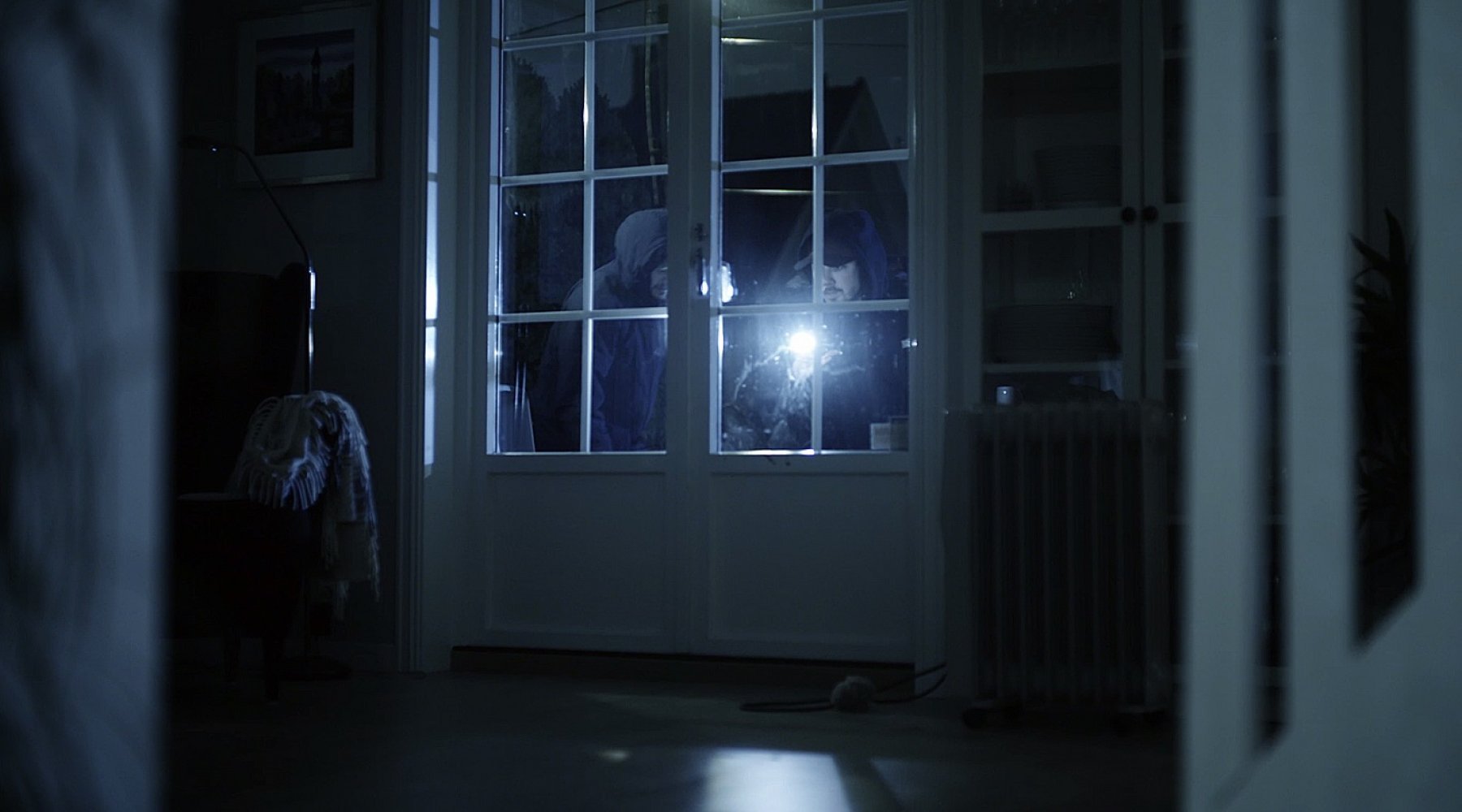 To innbruddstyver står utenfor en inngangsdør med lommelykt.