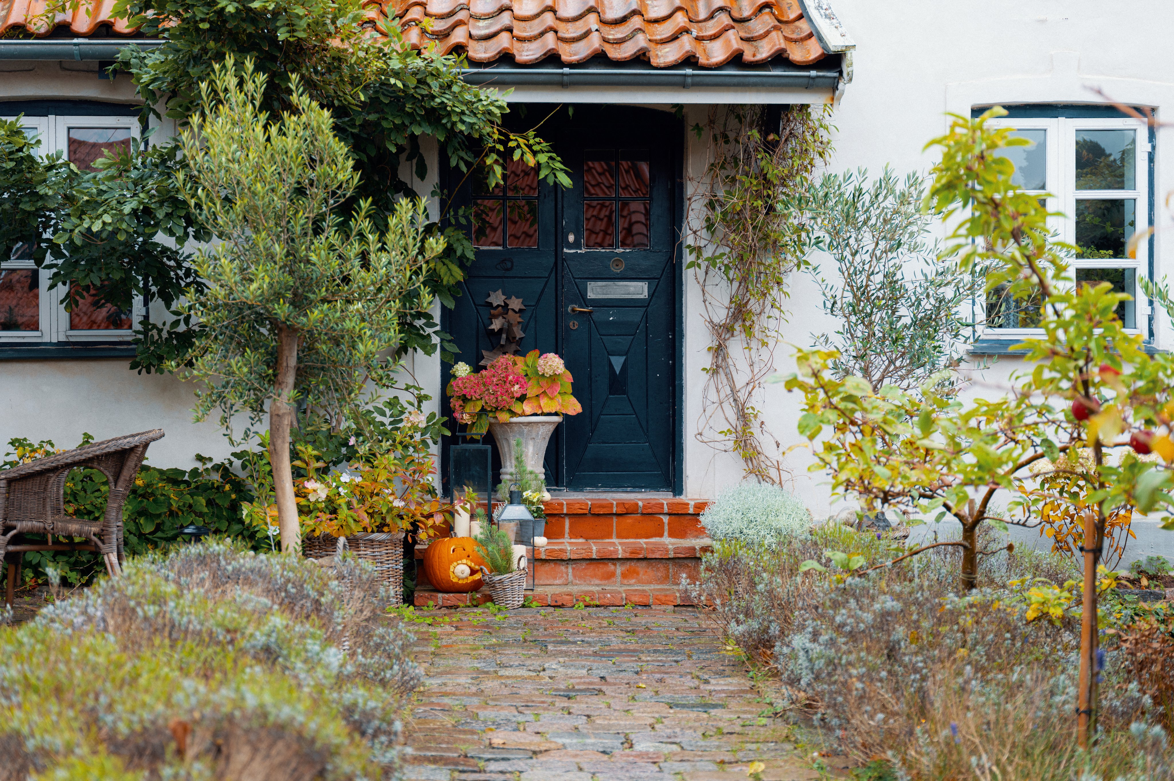 Inngangsparti til et hvitt murhus med trær og planter rundt.