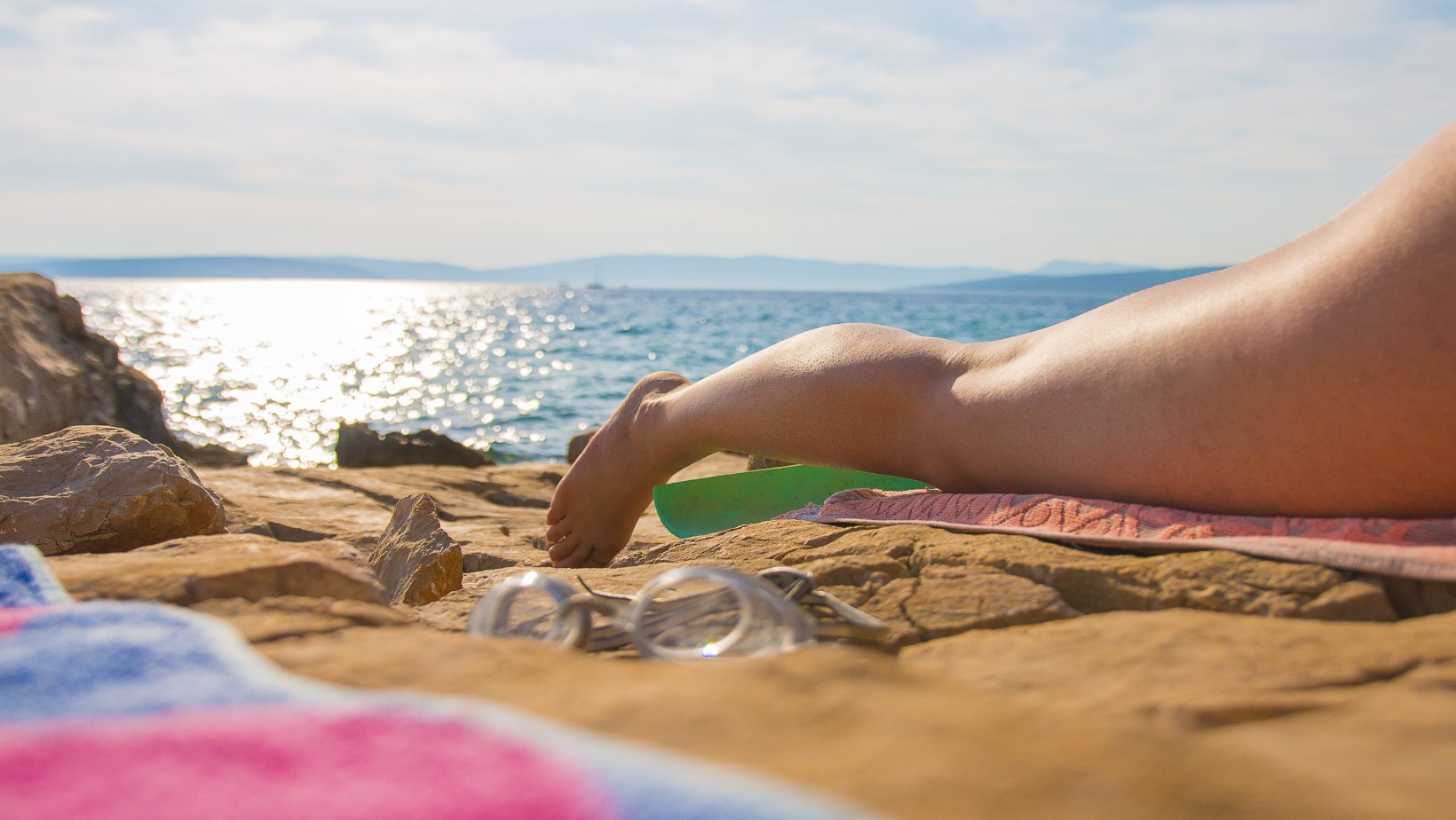 En kvinne ligger på en solfylt badestrand.