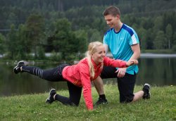 Dame står med venstre arm og høyre bein strukket ut. Treneren følger med.