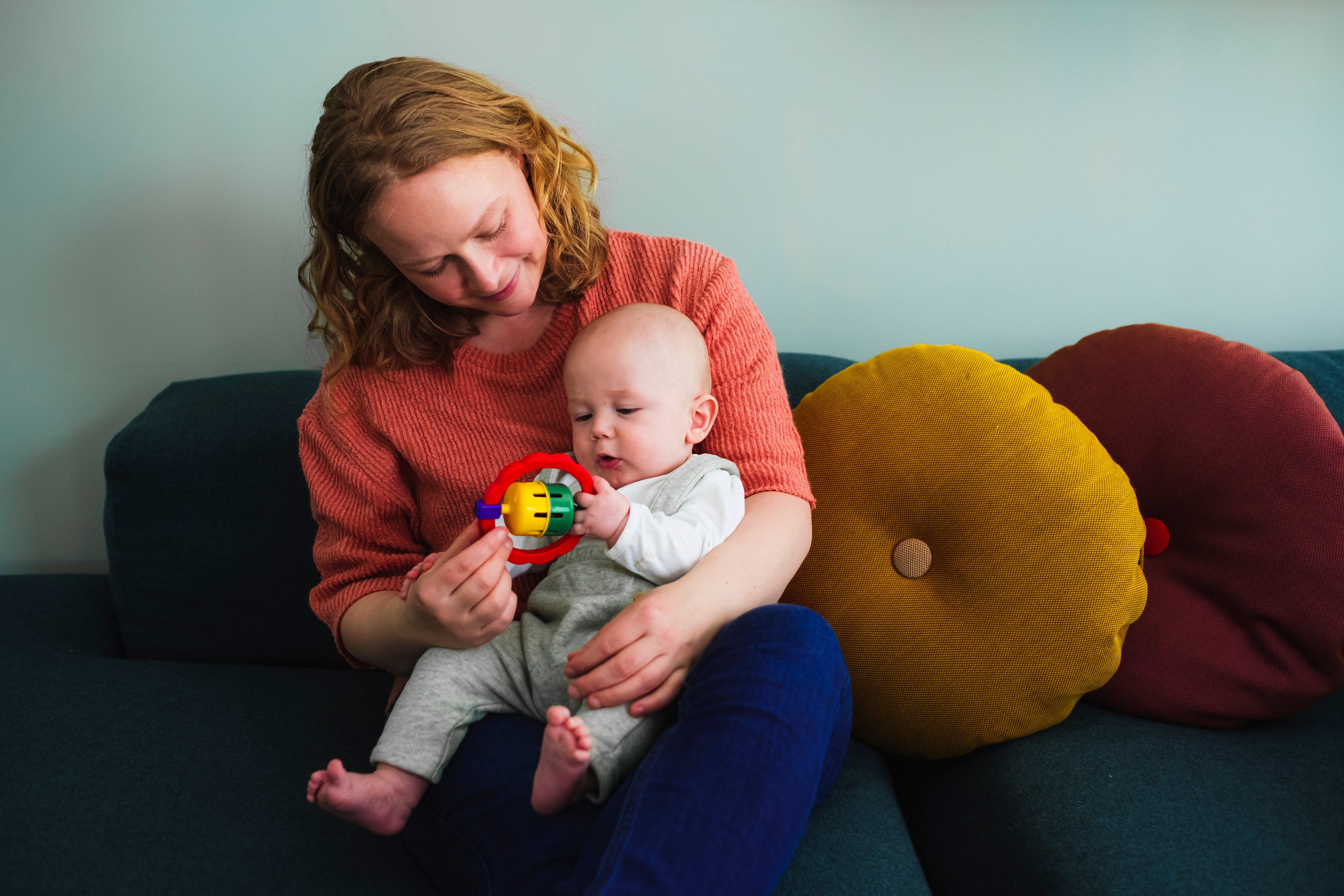 En mor holder babyen sin i fanget sitt mens hen holder en rangle.