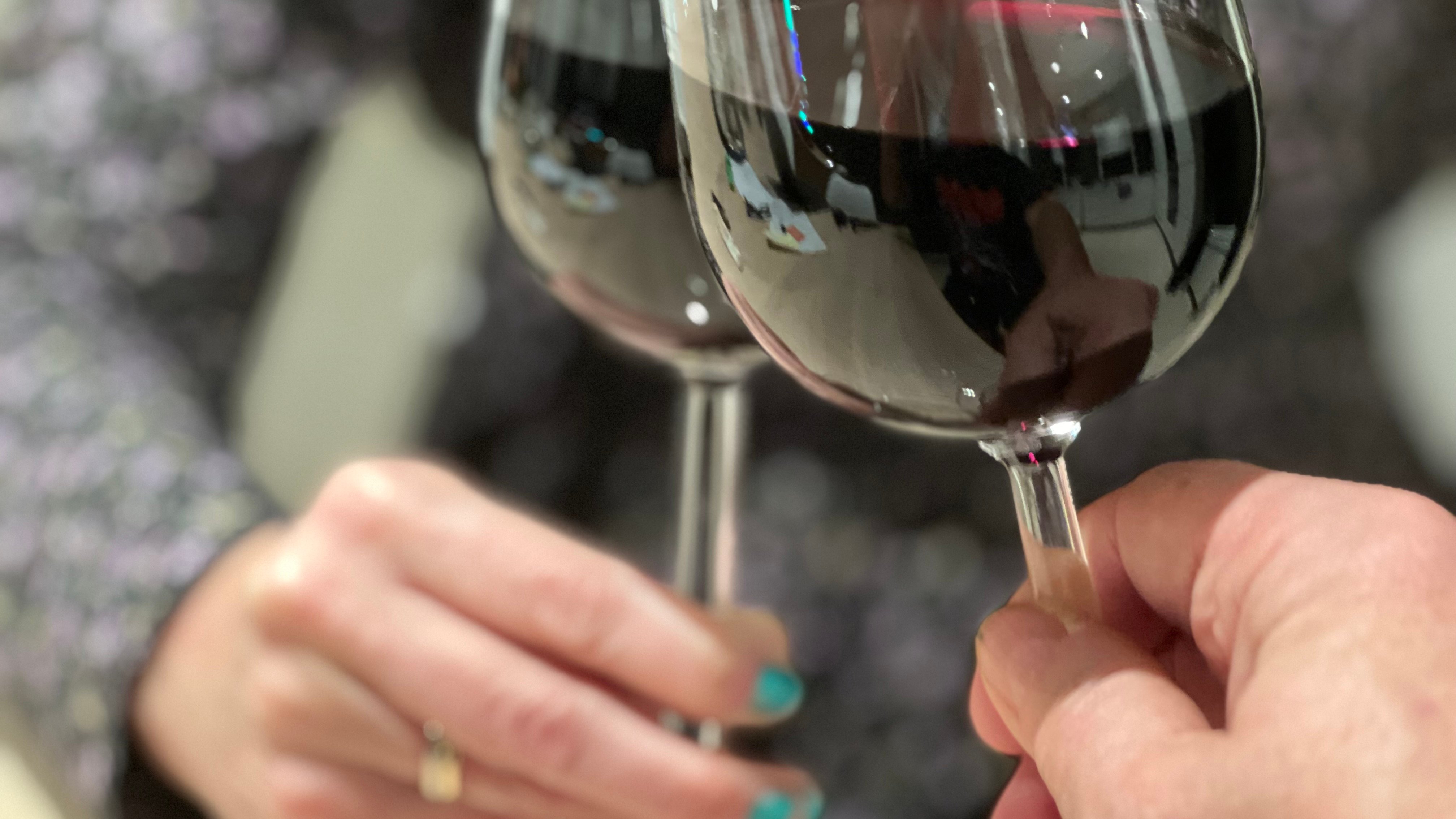 To vinglass med rødvin som møtes i en skål, holdt av to hender.