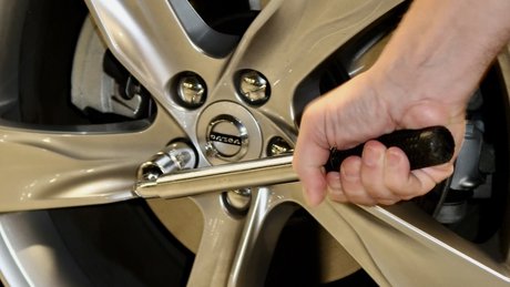 Hånd strammer en hjulmutter på en bilfelg med en skiftenøkkel.