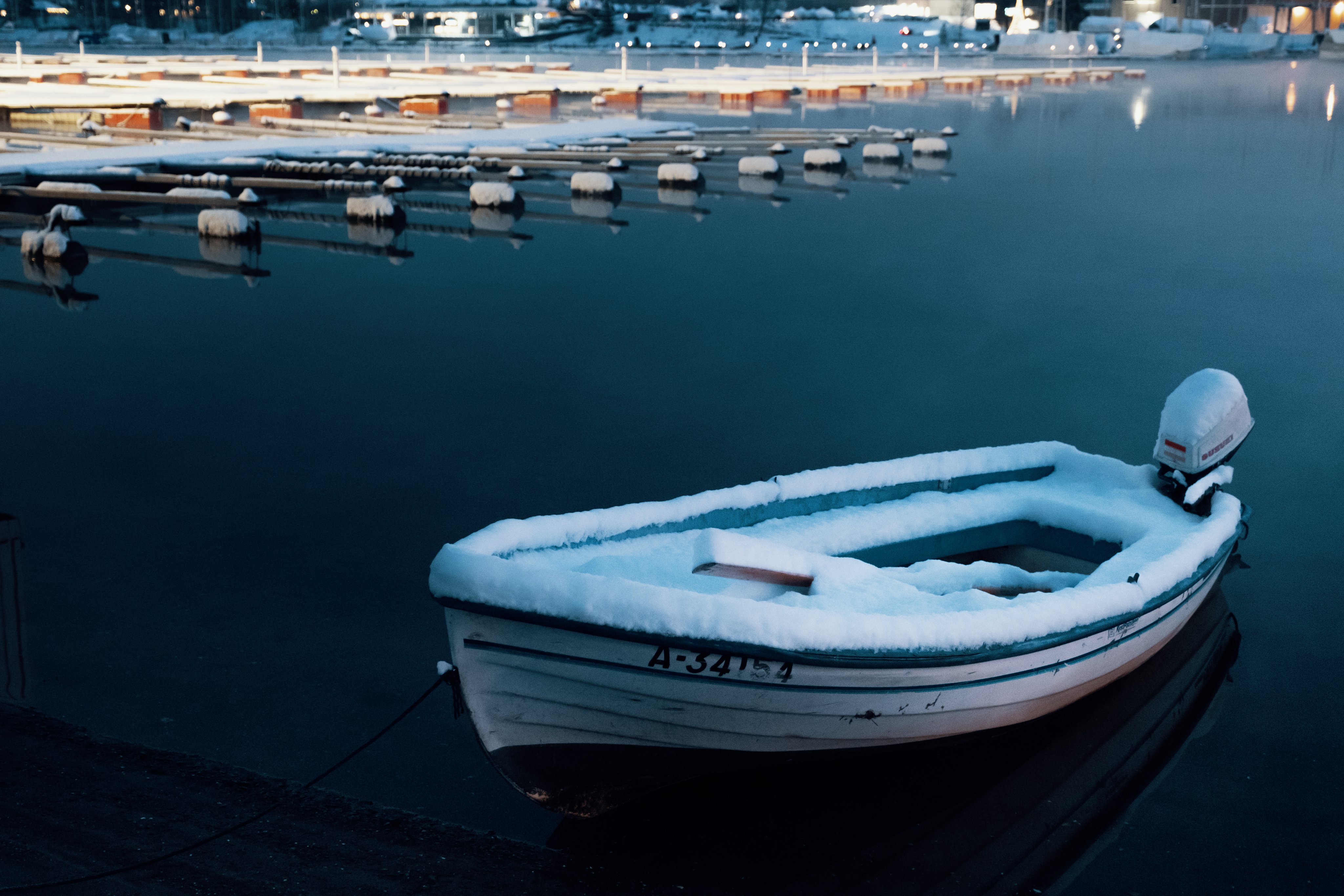 En liten snødekt båt ligger på vannet i en båthavn.