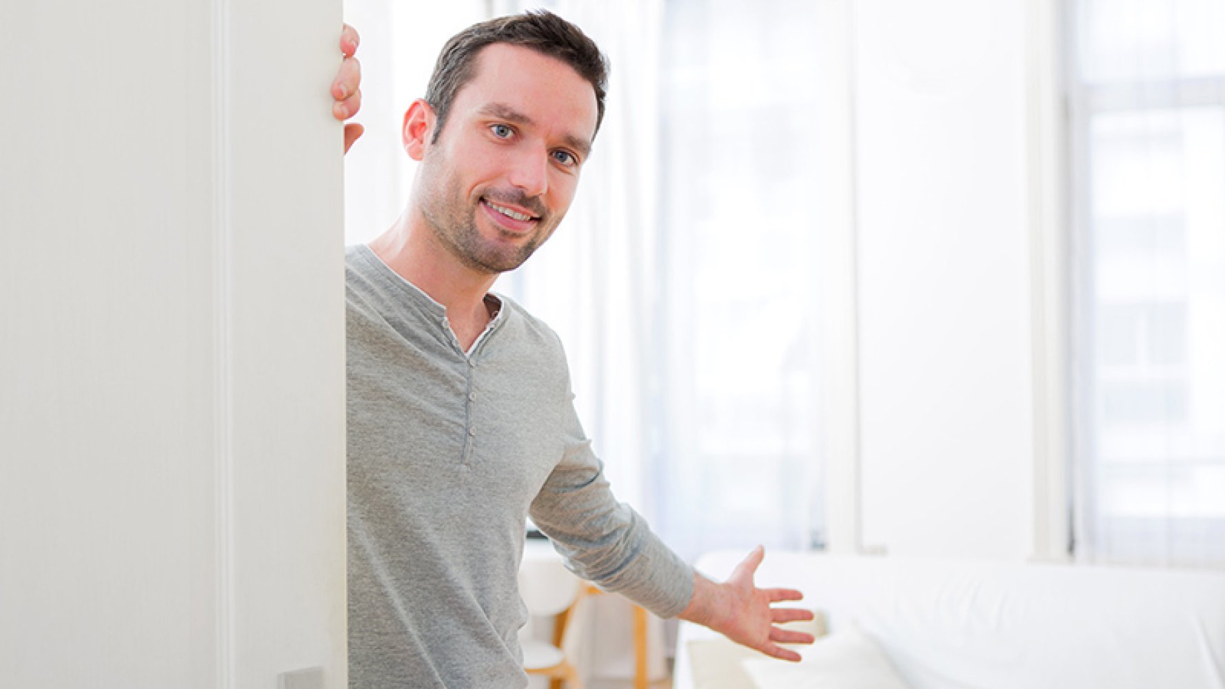 Mann holder inngangsdør åpen og inviterer inn.