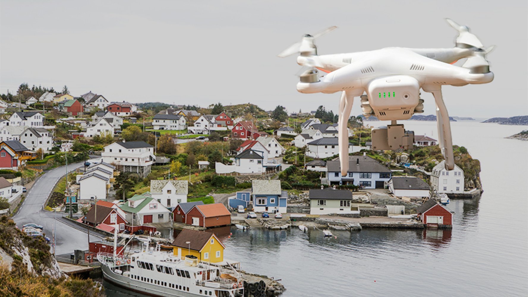 Drone flyr over en kystlandsby med fargerike hus og båter ved vannet.