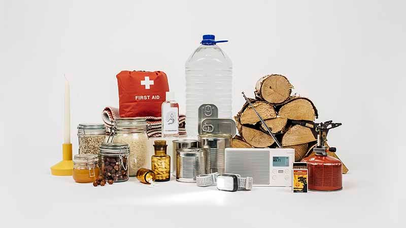 Samling av nødutstyr, inkludert vannflaske, førstehjelpspakke, hermetikk, vedkubber og lommelykt.
